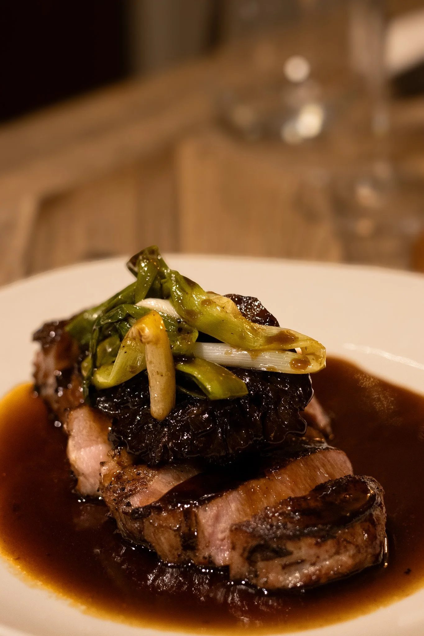 A close-up of a plated gourmet meal featuring a piece of cooked meat topped with vegetables and sauce. The Lamb Inn.