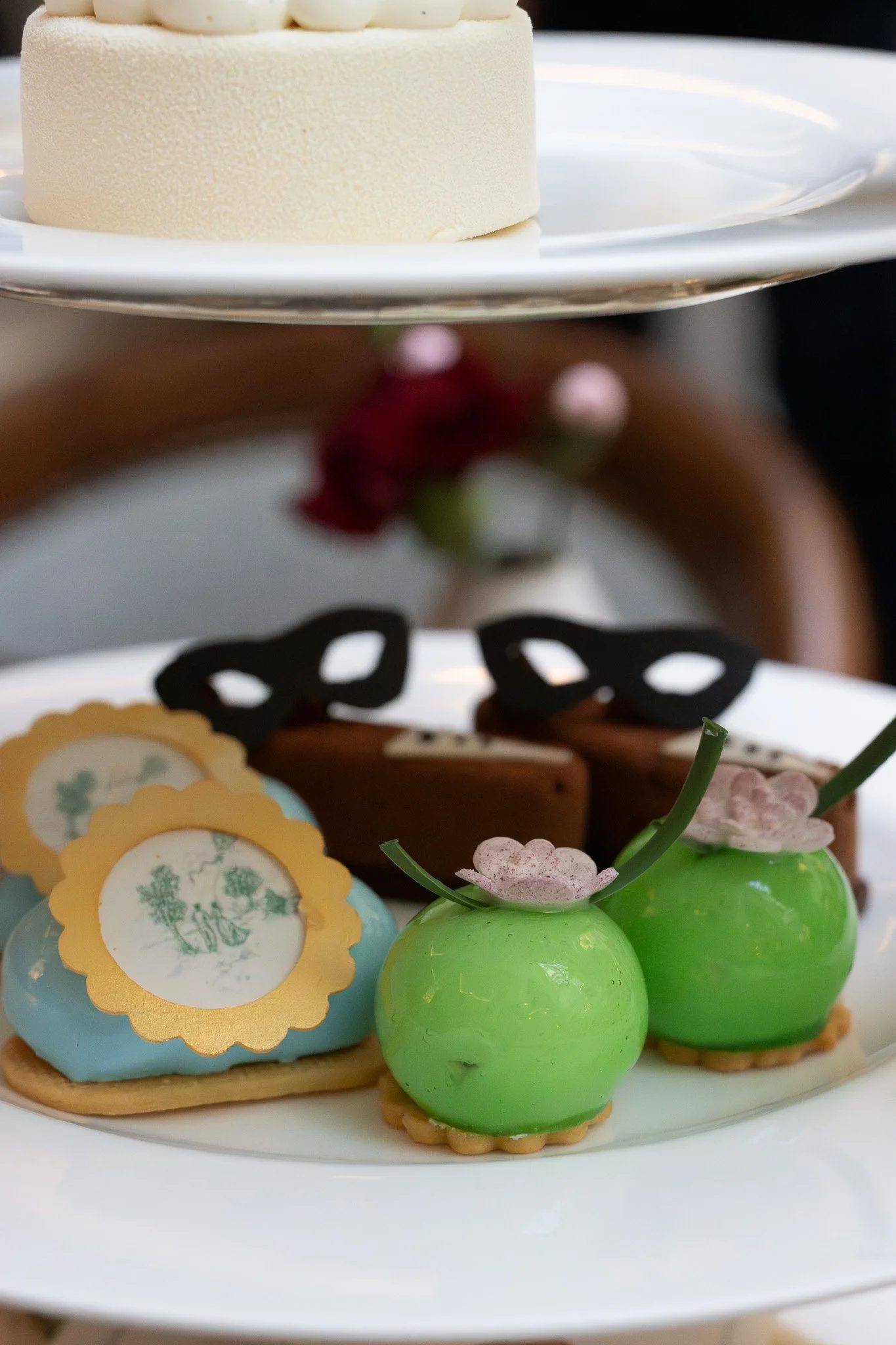 A white plate holding a white frosted cake decorated with white chocolate balls, with various decorated cookies and green and pink chocolate bunny figures around it. The Lanesborough. Bridgeton Afternoon Tea.